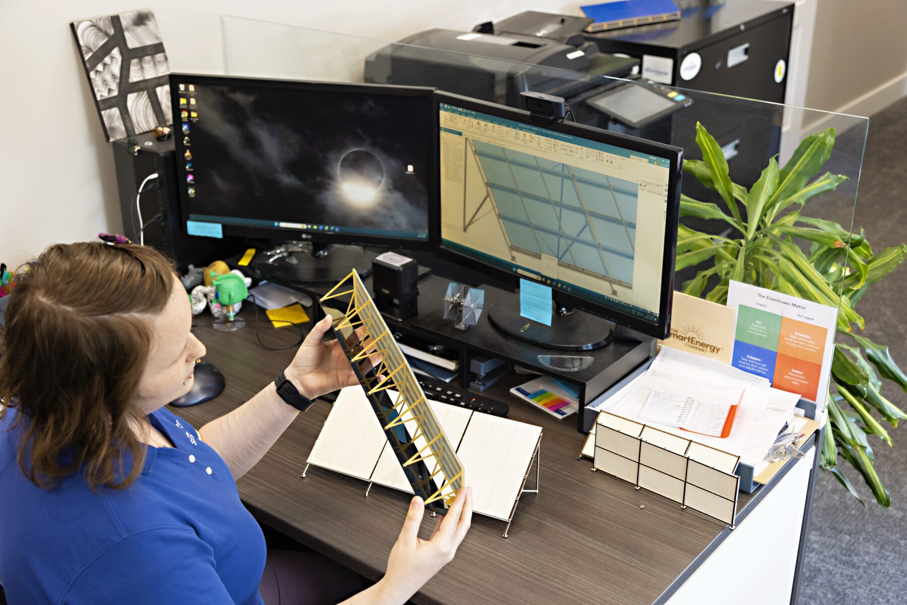 An engineering technologist from The Smart Energy Company looks at small-scale models of NOREASTER solar panels on her desk and on her computer screen.